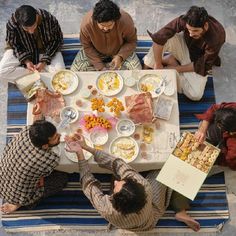 four people sitting at a table with food on it and one person holding an open book