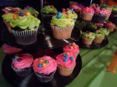 cupcakes are arranged on three tiered trays with colorful frosting and sprinkles