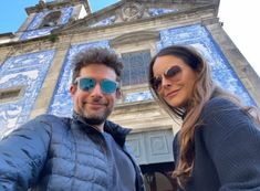 a man and woman taking a selfie in front of a building with blue tiles