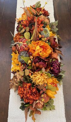 an arrangement of flowers is laid out on a white table runner with leaves and berries