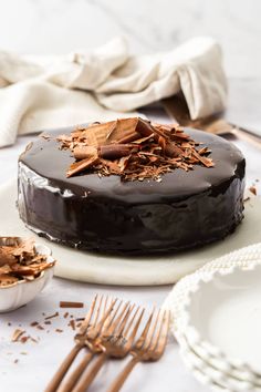 a chocolate cake sitting on top of a white plate next to two plates with forks