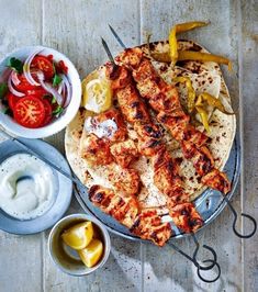 chicken kebabs on a platter with vegetables and dips