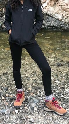 a woman standing in front of a river with her feet on the ground wearing hiking shoes