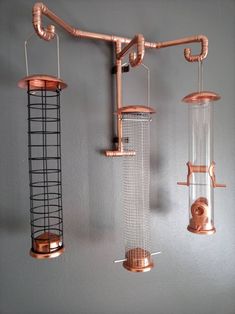 three bird feeders hanging from the side of a wall with wire and copper fixtures