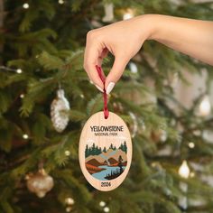 a hand holding a wooden ornament that says yellowstone national park in front of a christmas tree