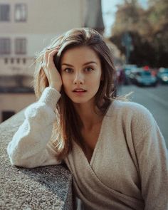 a woman leaning against a wall with her hand on her head and looking at the camera