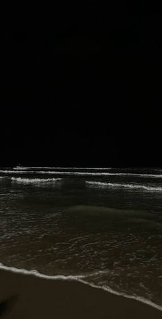 a person walking on the beach at night with their surfboard in hand and one foot in the water