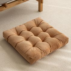 a square cushion sits on the floor in front of a coffee table