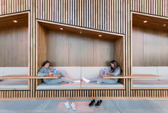 two women are sitting on benches in the middle of a room with wood paneling