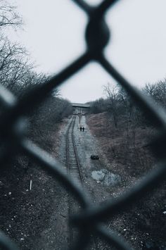 the view from behind a chain link fence looking down at a train track and trees