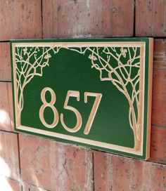 a green and gold house number sign mounted on a brick wall next to a tree