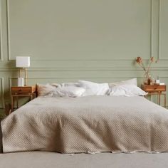 a bed with white sheets and pillows in a green room next to two nightstands