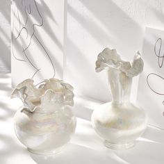 two glass vases sitting next to each other on a white tablecloth covered surface