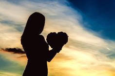 the silhouette of a woman holding a bouquet of flowers in front of a cloudy sky