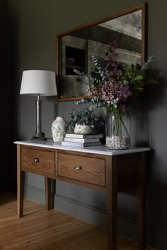 a wooden table topped with a vase filled with flowers and books next to a mirror