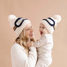 a woman holding a baby in her arms and wearing knitted hats with pom poms