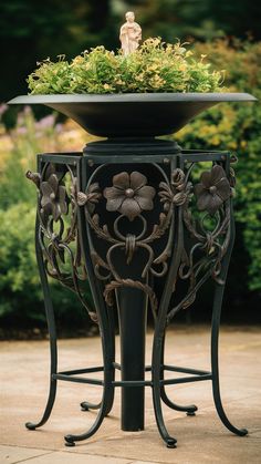 an iron plant stand with a potted plant in it's center and a small statue on top