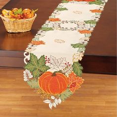 a table runner with pumpkins and leaves on it next to a basket of fruit