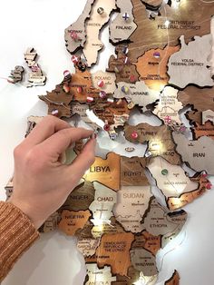 a person's hand pointing at a map made out of wood and metal pieces