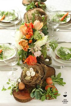 the table is set with flowers, eggs and carrots in nestes on wood slices