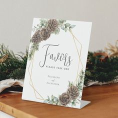 a place card with pine cones and greenery on it sitting on top of a wooden table