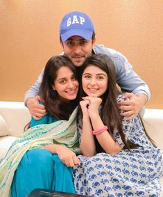 two women and a man sitting on a couch with their arms wrapped around each other