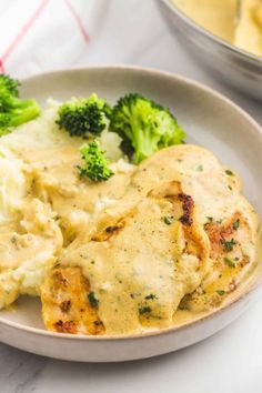 a white plate topped with chicken and broccoli covered in gravy next to a bowl of mashed potatoes