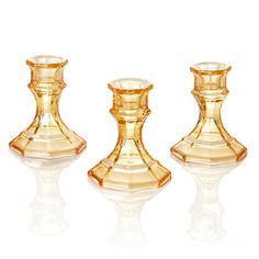 three glass candlesticks sitting next to each other on a white surface with reflections