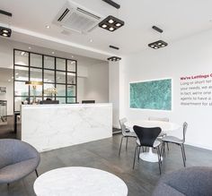 an office lobby with chairs, tables and a marble counter in front of the reception desk