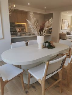 a dining room table with white chairs and a potted plant on the centerpiece