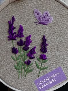 a close up of a embroidery on a piece of cloth with purple flowers and a butterfly