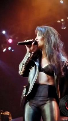 a woman standing on stage with a microphone in her hand and wearing black leather pants