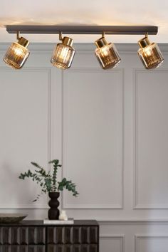 three lights are hanging from the ceiling above a dresser and table in a room with white walls