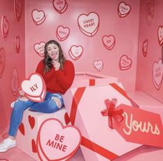 a woman sitting on top of a valentine's day gift box in a pink room