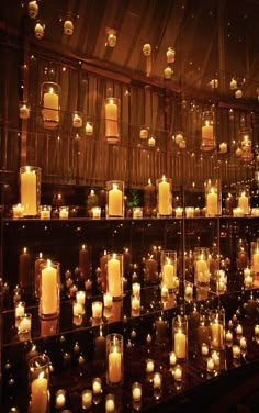 rows of lit candles are lined up against a wall in a room with glass walls