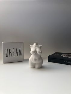 a white ceramic figurine sitting next to a book and a sign that says dream