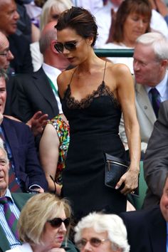 a woman in a black dress and sunglasses at a tennis match