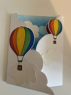 two hot air balloons floating in the sky on a cloud filled day with white clouds