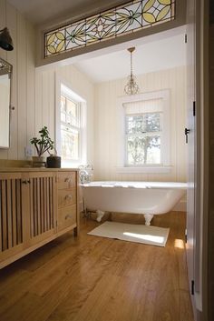 a white bath tub sitting next to a wooden cabinet in a bathroom on top of a hard wood floor