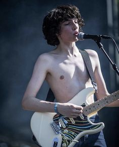 a shirtless young man playing an electric guitar on stage at a music festival or concert