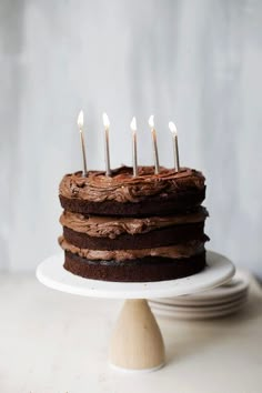 a chocolate cake sitting on top of a white plate with lit candles in the middle