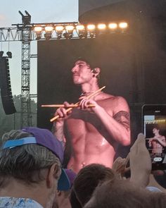 a man holding a bamboo stick in front of a large screen on a stage with people watching