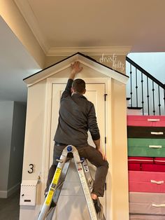 a man on a ladder painting the side of a house with drawers and stairs in front of him