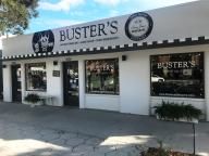 the outside of buster's restaurant with signs on it and trees in front of it