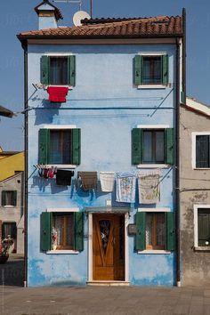 a blue building with green shutters and laundry hanging out to dry