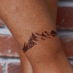 a tattoo on the leg of a woman with mountains and trees in the back ground