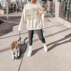 a woman walking her dog on a leash down the street while wearing a sweatshirt with an elephant print