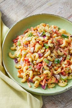 a green bowl filled with pasta salad on top of a wooden table next to a yellow napkin