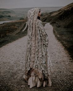 a woman wearing a veil standing on a gravel road in the middle of an open field