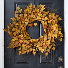 a wreath with yellow and red leaves is hanging on the front door's black door